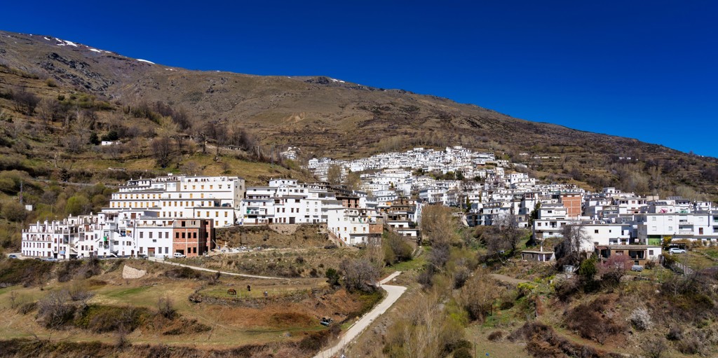 Wit bergdorp in de Sierra Nevada bij Granada, Spanje, met kronkelende weg en heuvels op de achtergrond.