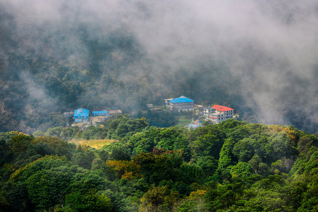 Kleurrijke lodges in de mist boven een groen bergbos tijdens een 22-35ers reis Nepal.