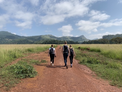 Wandelaars op een rode zandweg door het groene landschap van Zuid-Afrika, met bergen op de achtergrond.