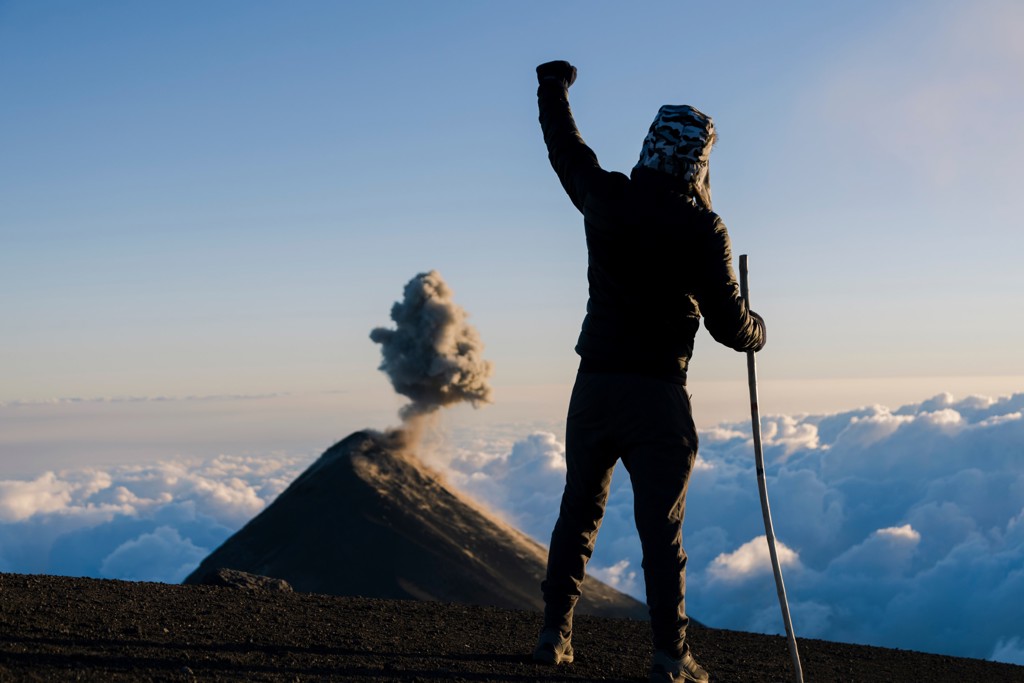 Wandelaar op vulkaantop met wandelstok, met rokende vulkaan boven de wolken tijdens 22-35ers reis Guatemala.