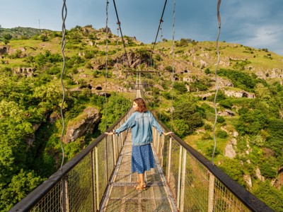 Reiziger op een hangbrug met uitzicht op groene heuvels en rotsformaties tijdens de route Armenië en Georgië.