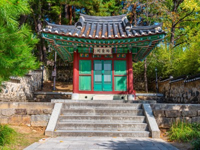 Traditioneel Koreaans tempelgebouw met groen-rode details tussen bomen, op de route door Zuid-Korea.