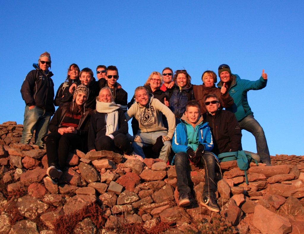 Familiegroep op een rotsachtige heuvel tijdens familiereis Peru, met duim omhoog bij zonsondergang.