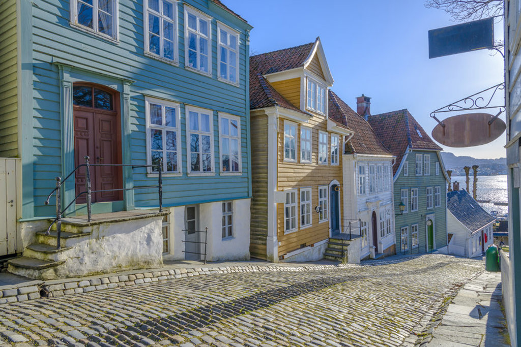 Kleurrijke houten huizen aan een geplaveide straat in Bergen, Noorwegen, met uitzicht op het water.