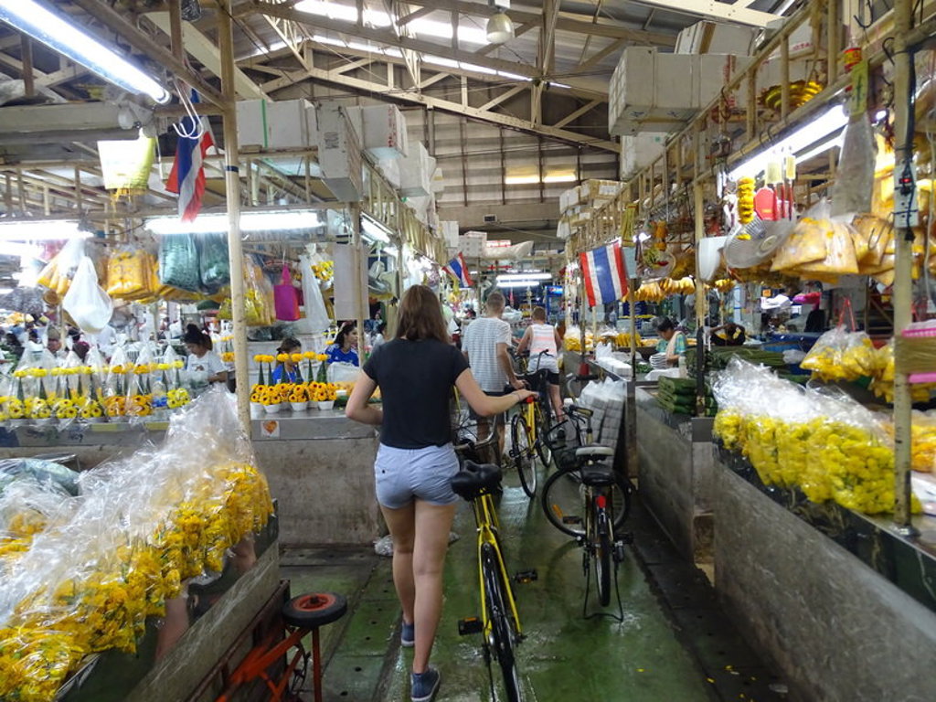 Fietstocht door een overdekte markt in Thailand tijdens een familiereis, langs bloemen en kraampjes.