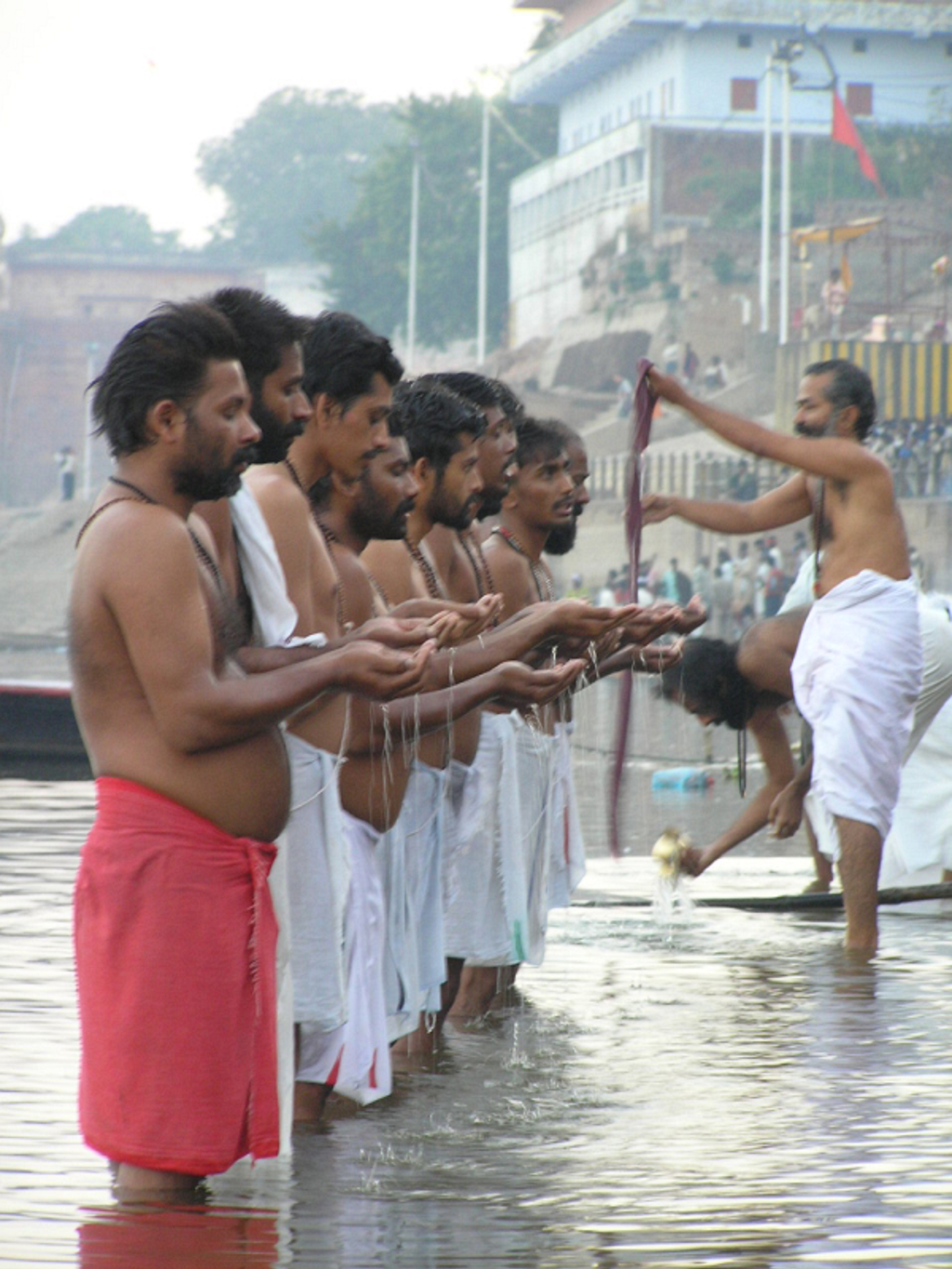 Hindoeritueel aan de rivier in India, met mannen die bidden en water offeren bij de ghats.