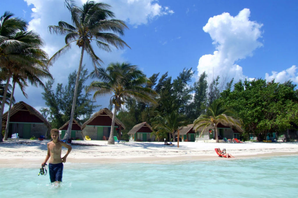 Tropisch strand in Cuba met palmbomen, strandhuisjes en kinderen in het heldere water.