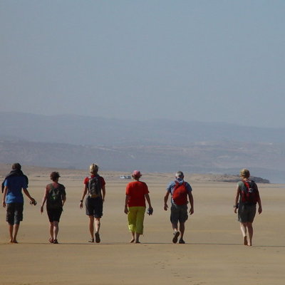 Groep reizigers wandelt over een uitgestrekt zandstrand in Marokko tijdens een groepsrondreis.
