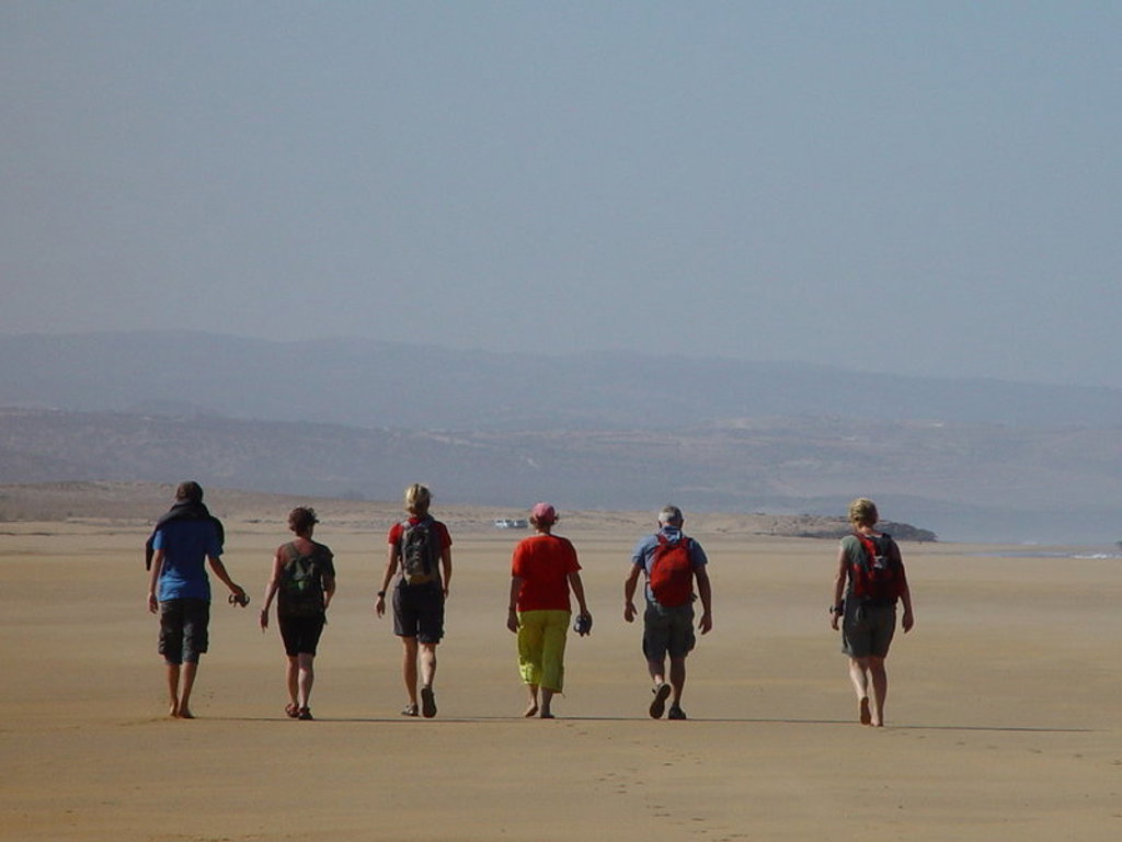 Groep reizigers wandelt over een uitgestrekt zandstrand in Marokko tijdens een groepsrondreis.