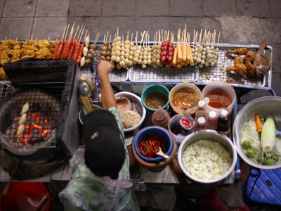 Straatkraam met gegrilde spiesjes, sauzen en verse groenten op een avondmarkt in Thailand.