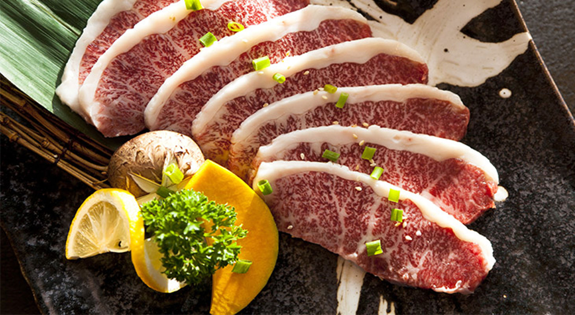 Wagyû beef in Japan Dun gesneden wagyu rundvlees op een schaal, gegarneerd met lente-ui, citroen en peterselie.