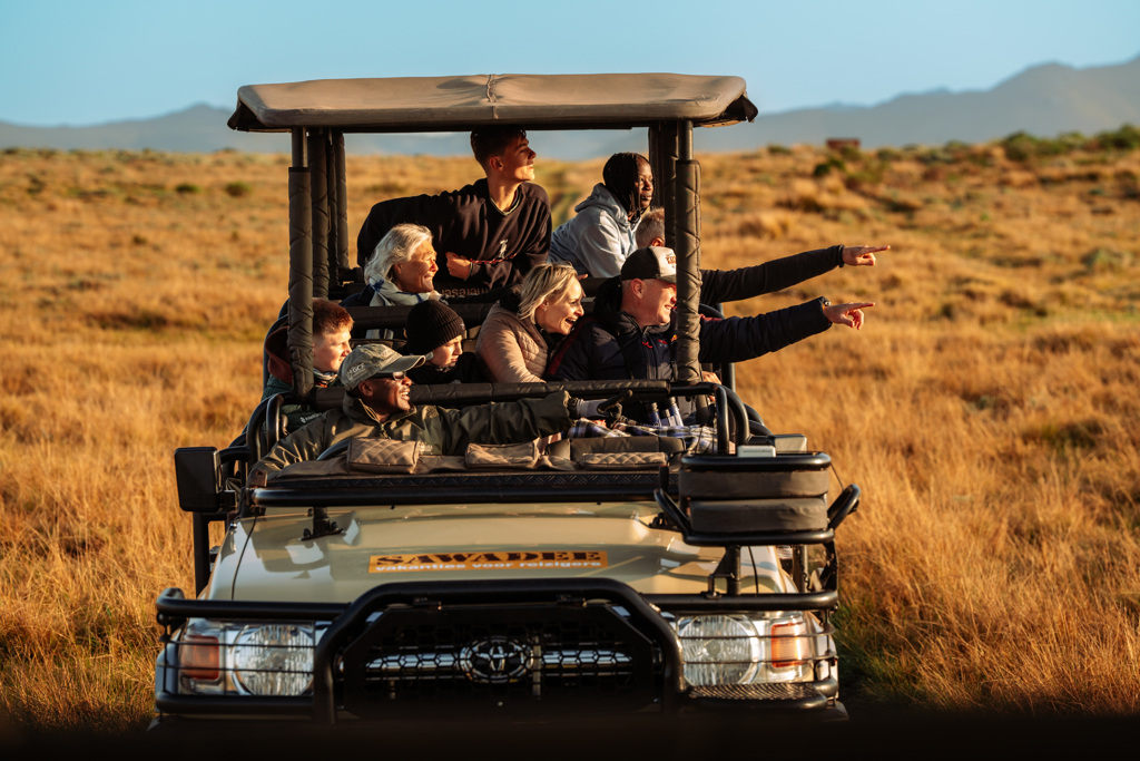 Gezin op safari in open jeep in Zuid-Afrika, wijzend naar wild op de savanne.