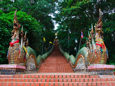 Trap naar een Thaise tempel, geflankeerd door kleurrijke naga-slangbeelden in het groen.
