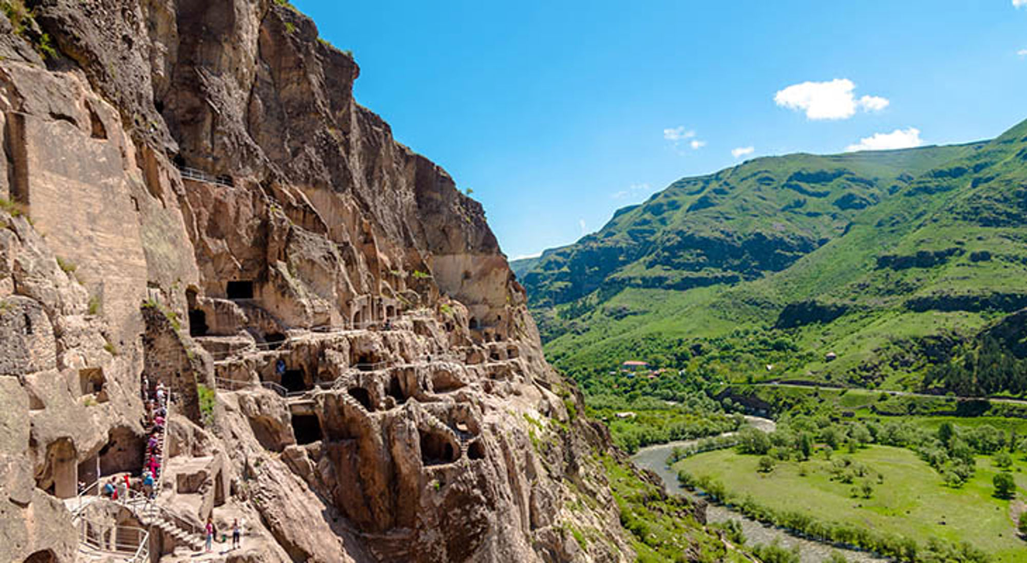 Grotstad Vardzia Uplistsikhe rotsstad met uitgehakte grotwoningen langs een klif, met uitzicht op een groene vallei en rivier.