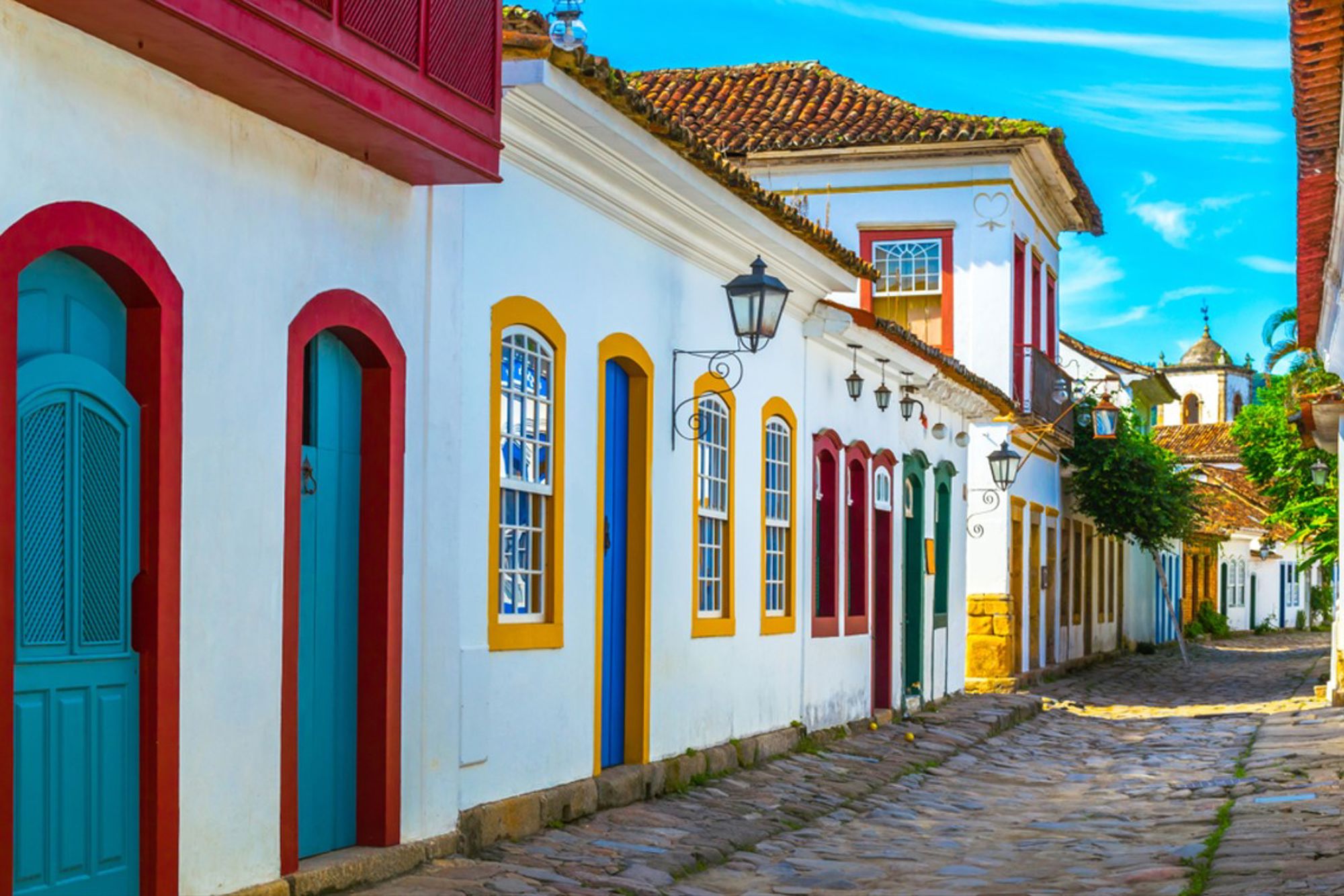 Kleurrijke koloniale straat in Paraty, Brazilië, met witgekalkte huizen en kasseien onder een blauwe lucht.