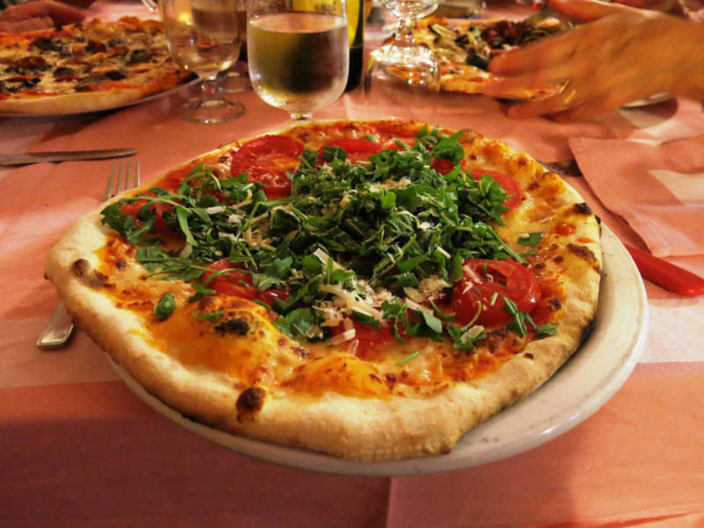 Pizza met tomaat, rucola en Parmezaanse kaas op tafel tijdens een wandelvakantie op Sardinië, Italië.