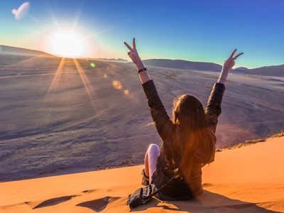 Reiziger op zandduin bij zonsopkomst in de Namib-woestijn, route Windhoek naar Victoria Falls.