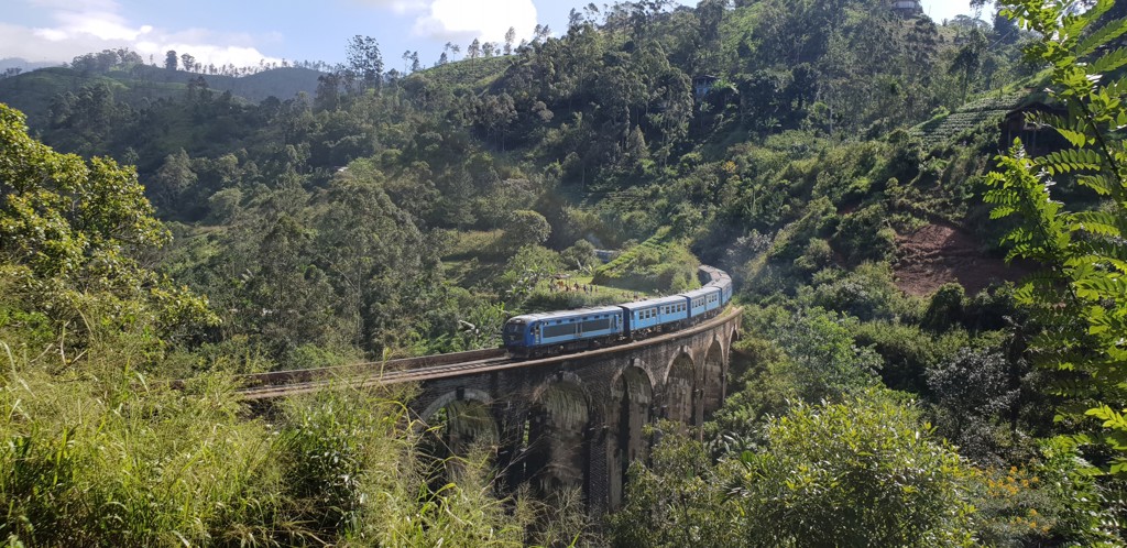Blauwe trein op de Nine Arch Bridge tussen groene heuvels in Sri Lanka.