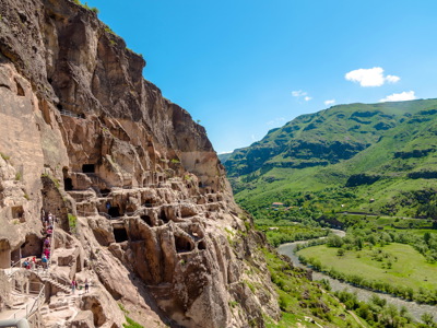 Uplistsikhe grottenstad in Georgië, uitgehouwen in rotswand met uitzicht op groene vallei en rivier.