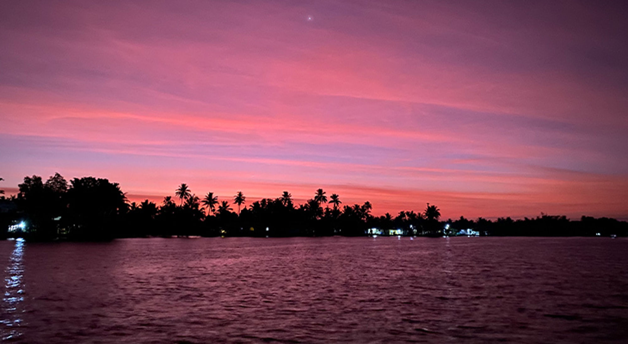 Roze zonsondergang boven een rustige rivier met silhouetten van palmbomen langs de oever.