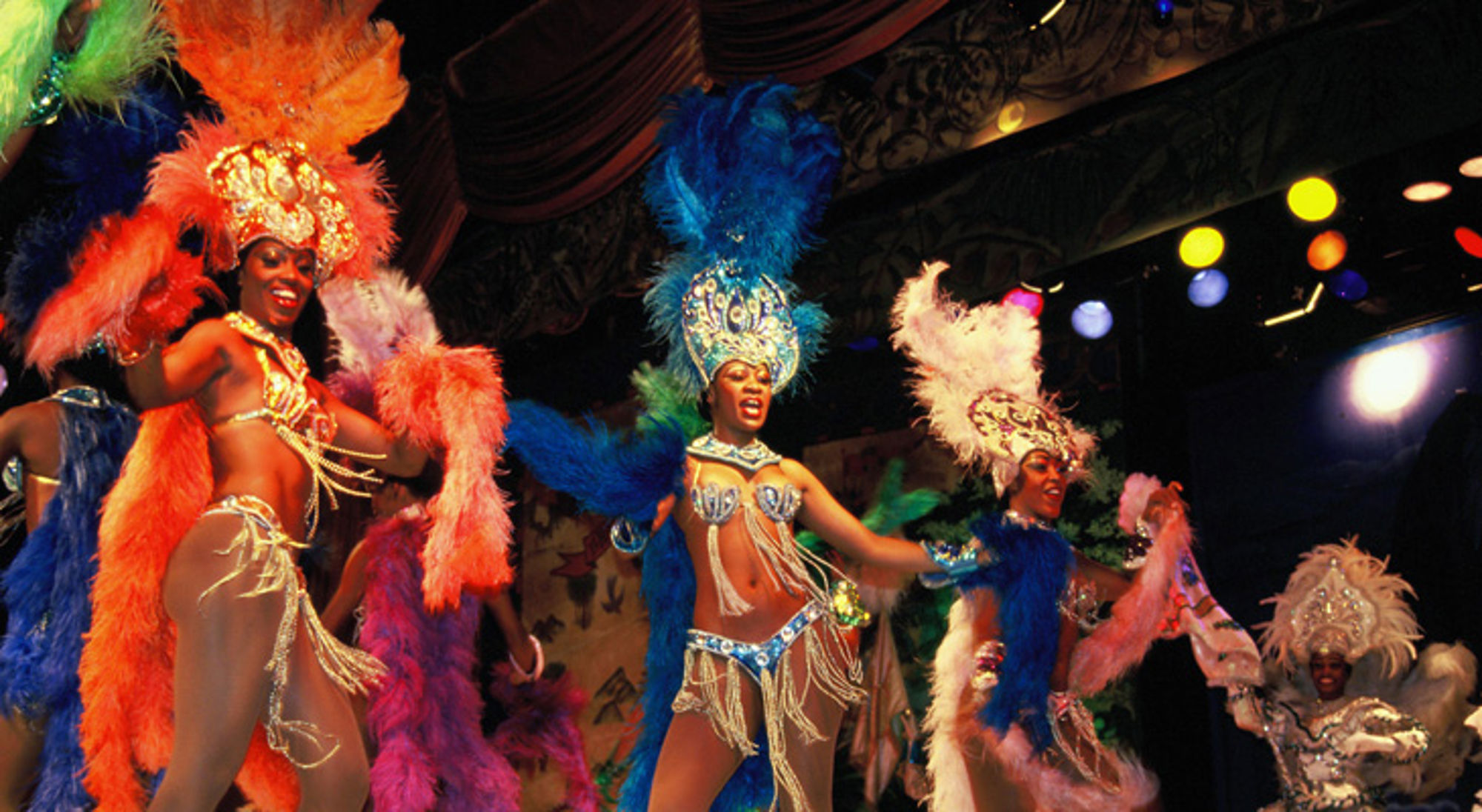 Showgirls dansen op het podium in kleurrijke veren kostuums tijdens een revue.