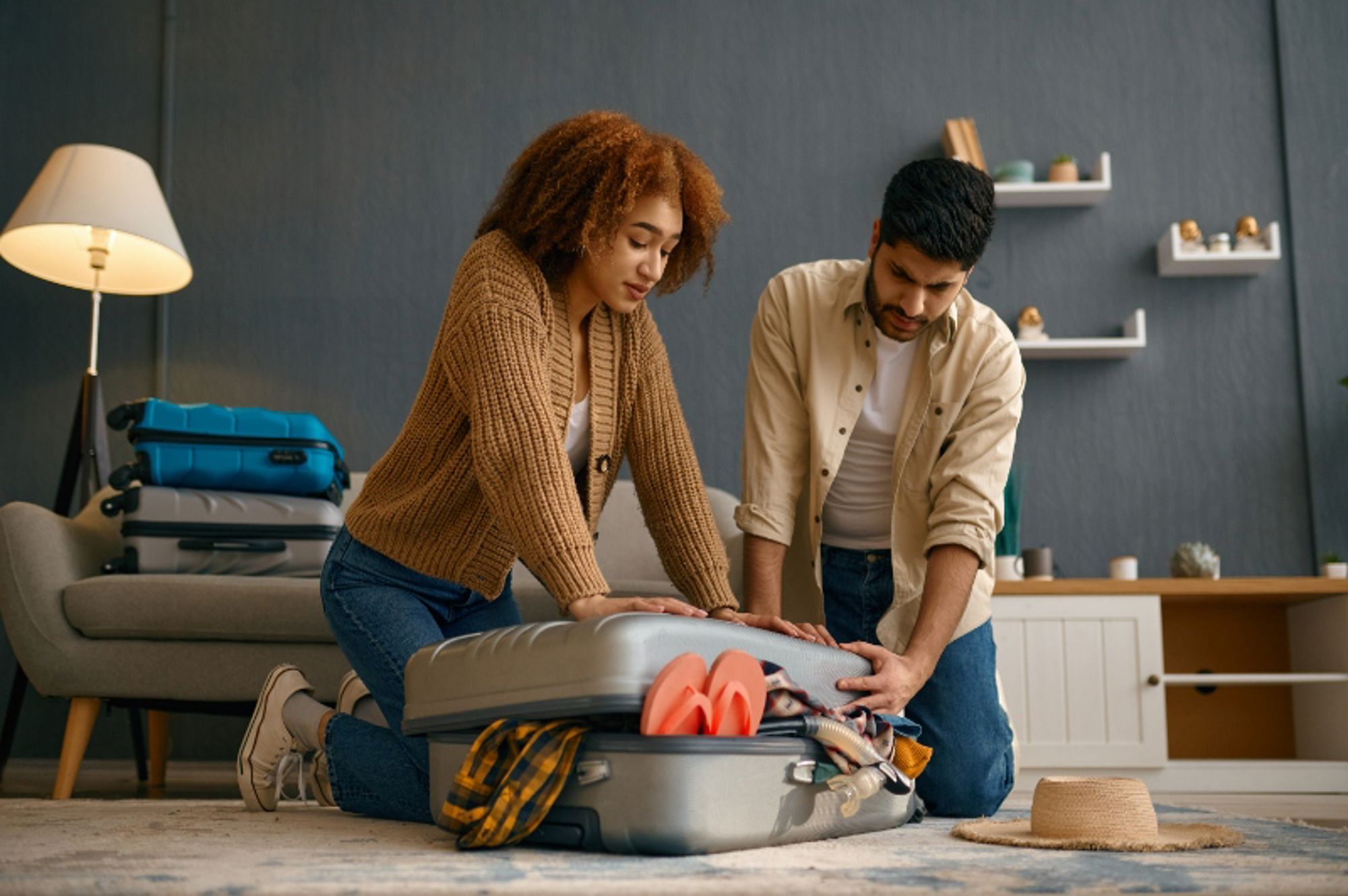 Koppel dat een overvolle koffer dichtdrukt tijdens het inpakken voor een vakantie.