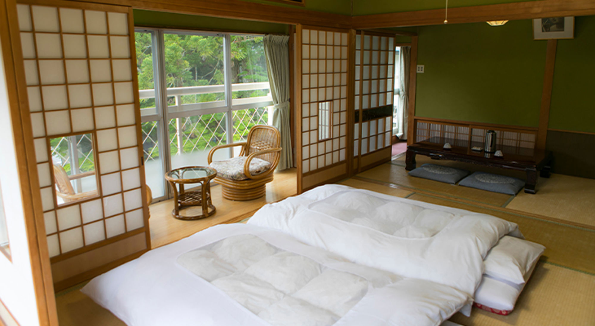 Ryokan Japan Traditionele Japanse kamer met tatami, futonbedden en shoji-schuifdeuren, met uitzicht op groen vanaf het balkon.