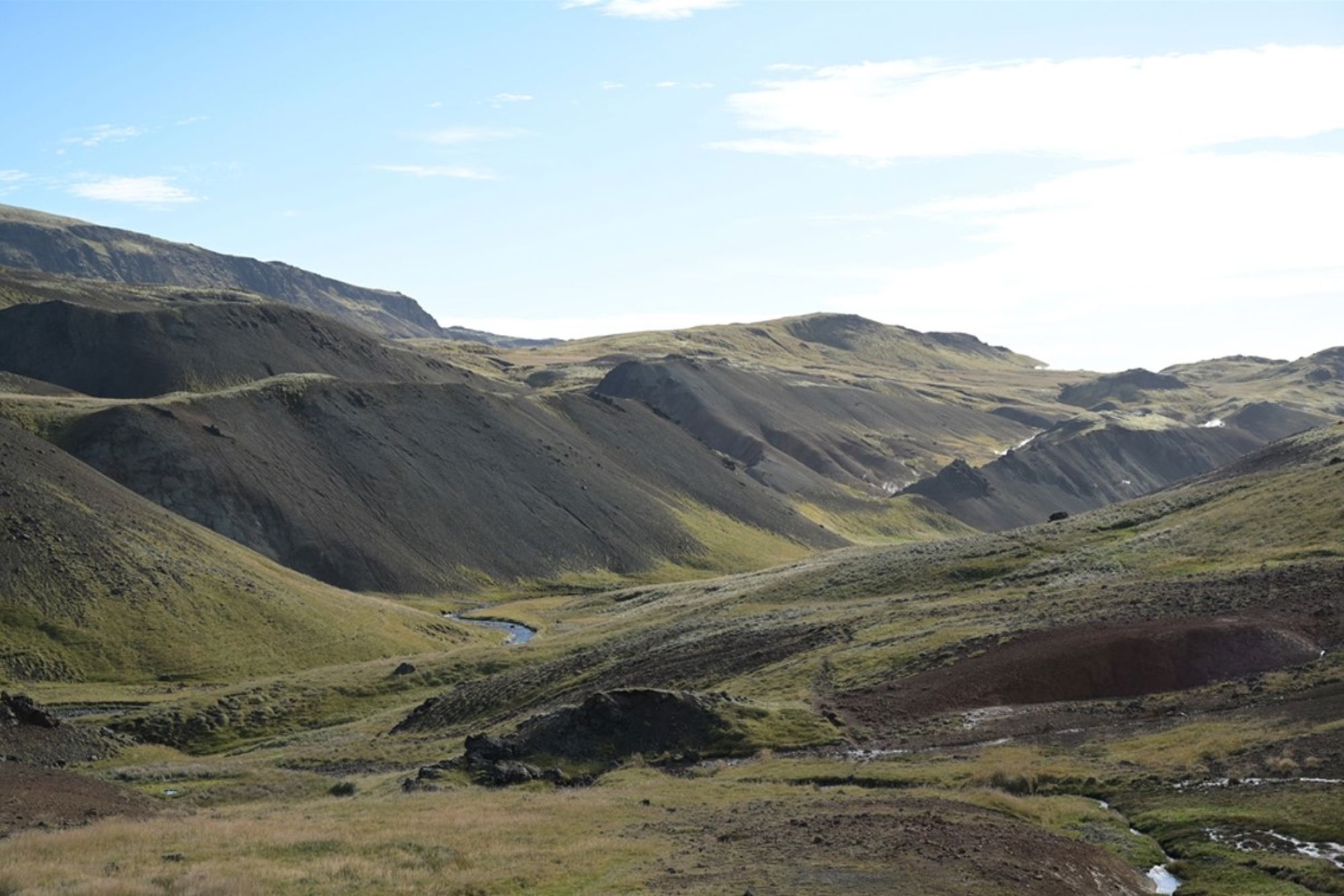 Groene heuvels en vulkanisch landschap in IJsland met een beekje door de vallei.