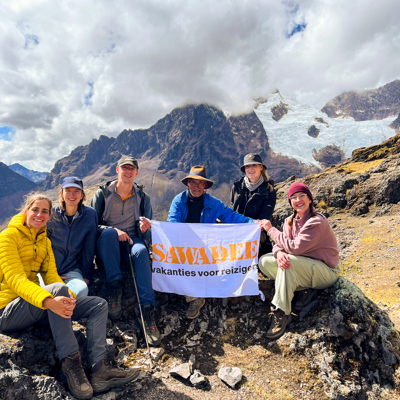 Groep 22-35ers wandelaars in de Peruaanse Andes met Sawadee-vlag, met besneeuwde bergtoppen op de achtergrond.