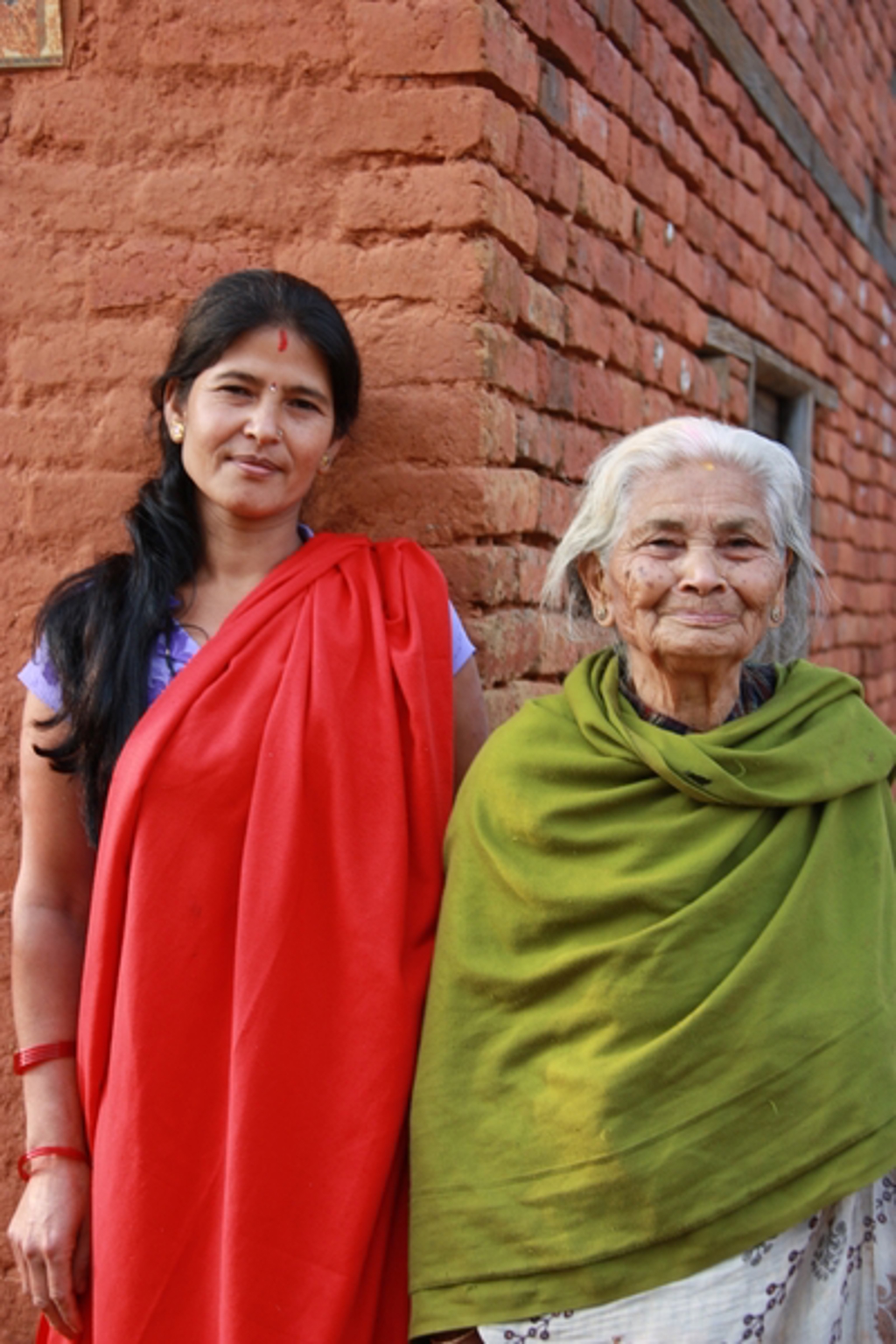 Twee Nepalese vrouwen in kleurrijke doeken voor een rode bakstenen muur.