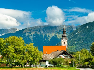 Kerk met klokkentoren in Sloveens dorp, met de Julische Alpen op de achtergrond.