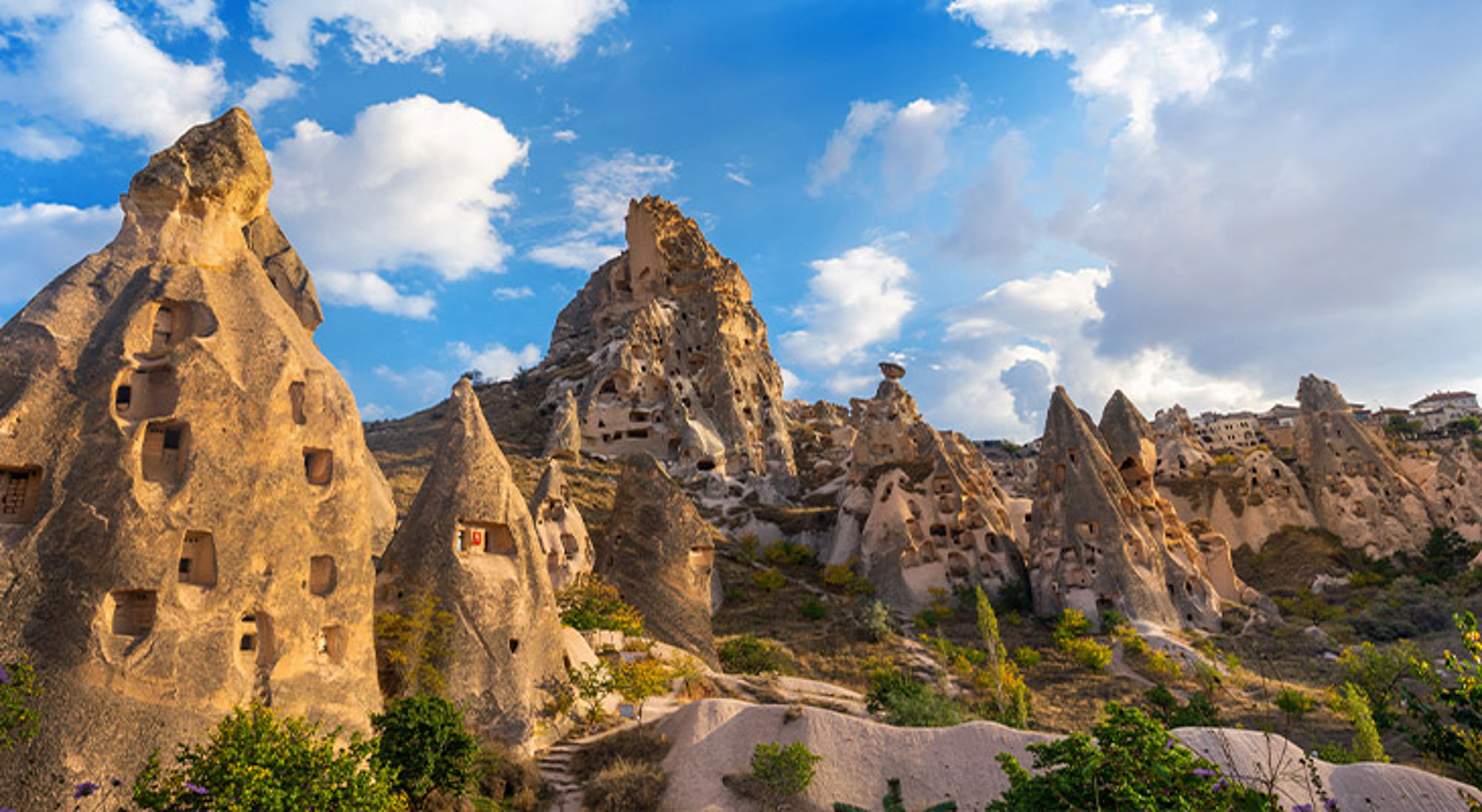 Rotsformaties met uitgehakte grotwoningen in Cappadocië onder een blauwe lucht met wolken.
