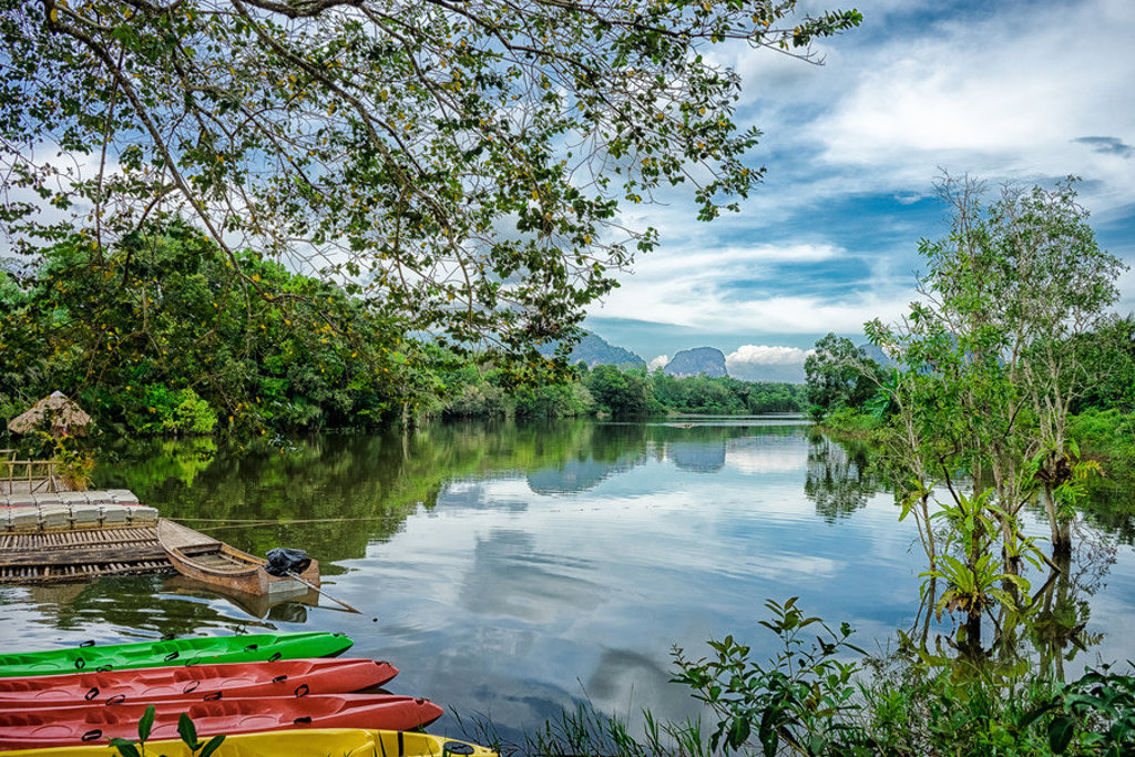 Kajaks aan de oever van een rustige rivier in Thailand, omringd door jungle en bergen tijdens de familiereis Chill & Adventure.