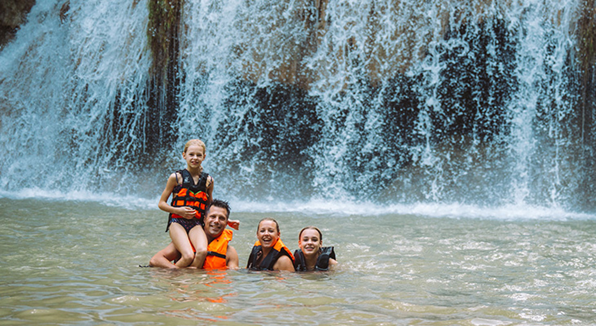 Familiereis Thailand Gezin zwemt met zwemvesten bij een waterval in een natuurlijke lagune.
