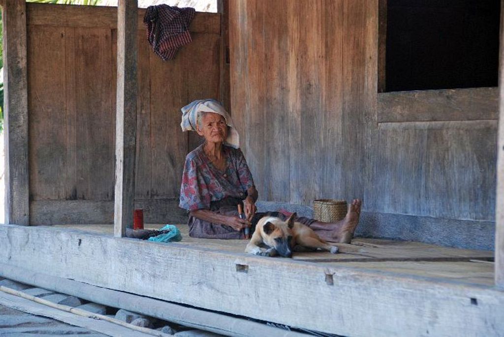 Oude vrouw op houten veranda met hond op de Kleine Sunda eilanden, Indonesië.