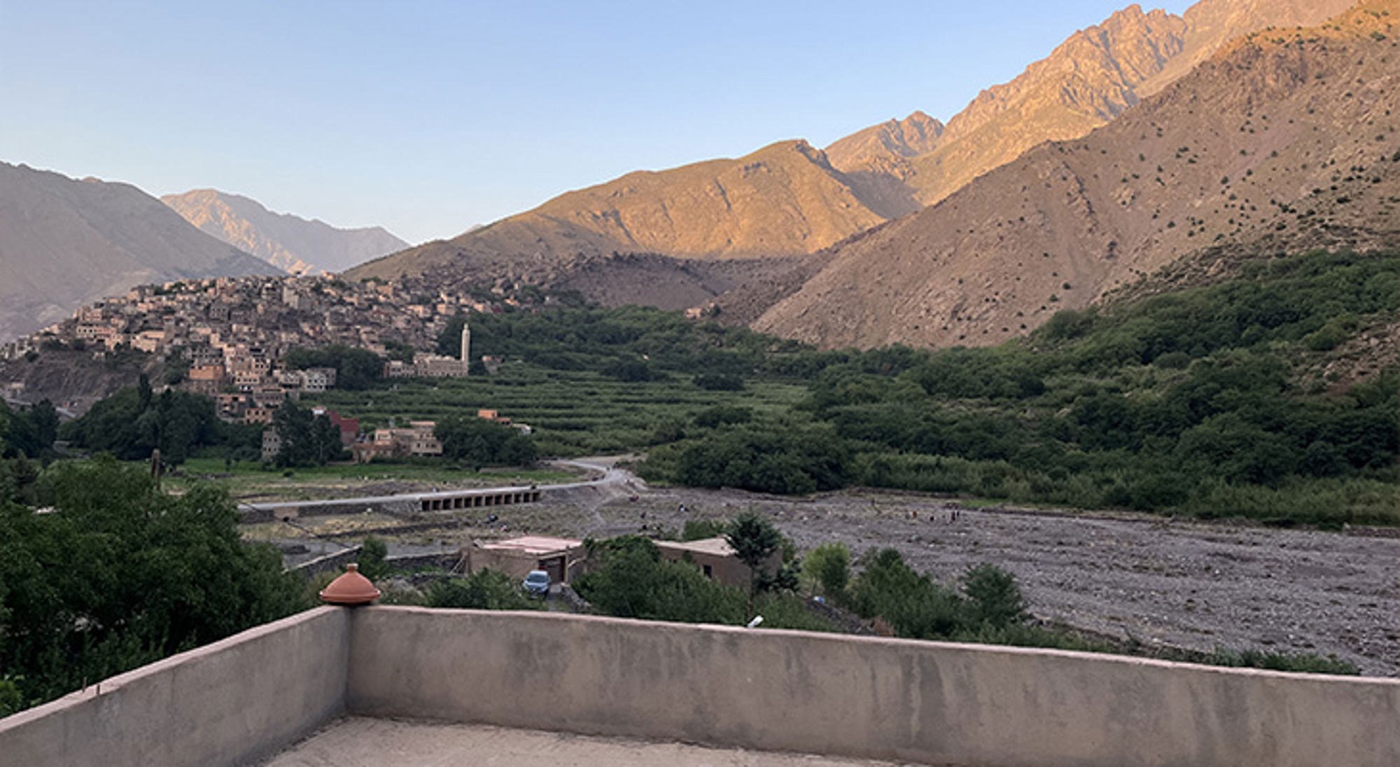 Uitzicht Marokko Uitzicht op een bergdorp met minaret, groene vallei en rivierbedding tussen ruige bergen.