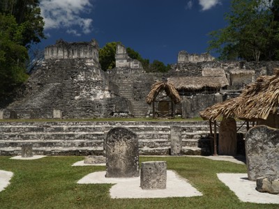 Maya-ruïnes van Tikal in Guatemala met stenen tempels en stèles op een groen plein.