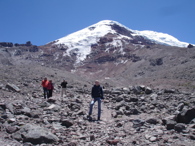 Wandelaars op rotsig pad met besneeuwde vulkaan op de achtergrond in Ecuador.