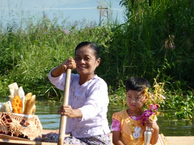 Vrouw en kind in boot op het Inlemeer in Myanmar, met bloemen en etenswaren aan boord.