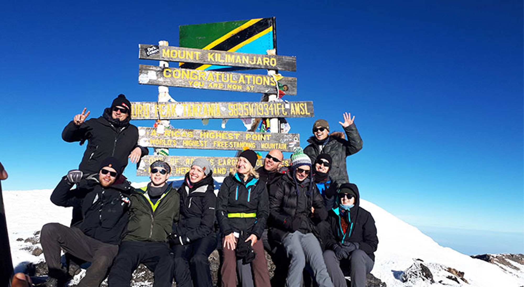 Groep wandelaars poseert bij het Uhuru Peak-bord op de top van de Kilimanjaro in Tanzania.