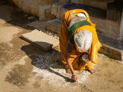 Vrouw in sari tekent een kolam met krijt voor een huis in Zuid-India.