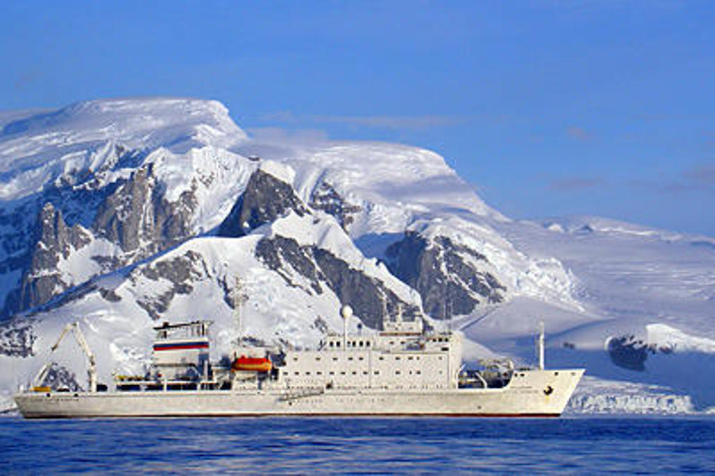 Expeditiecruiseschip in Antarctica voor de Zuidpoolcirkel, met besneeuwde bergen op de achtergrond.