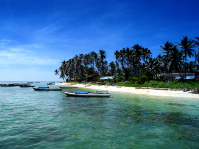 Tropisch strand op Kalimantan met palmbomen en bootjes in helderblauw water.
