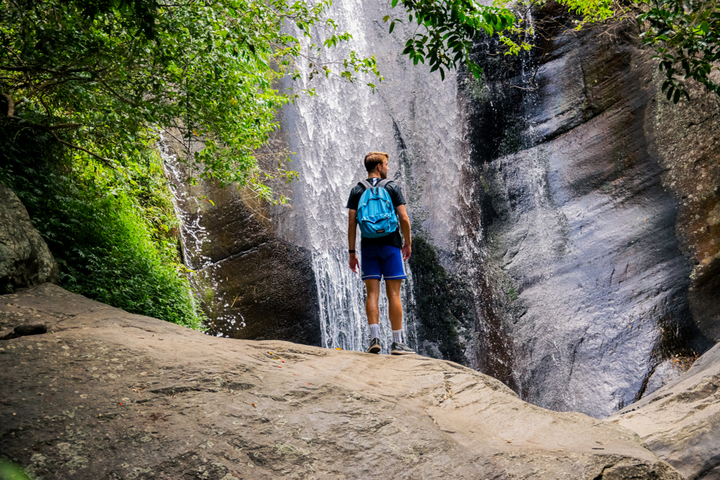 Jonge reiziger met rugzak bij een waterval in de jungle tijdens een 22-35ers reis Sri Lanka.