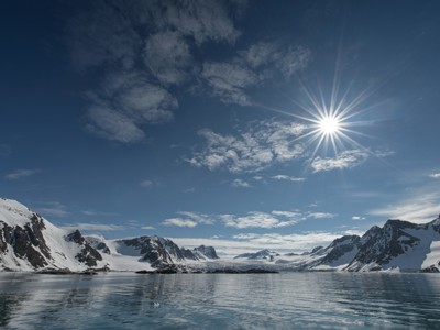 Zon boven een fjord met besneeuwde bergen en gletsjers op Spitsbergen.