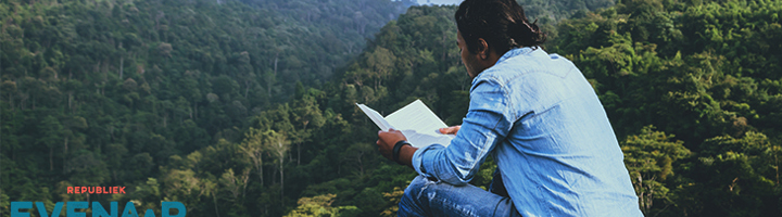 Man leest een boek met uitzicht op groen berglandschap, inspirerend voor boekentips voor op vakantie.