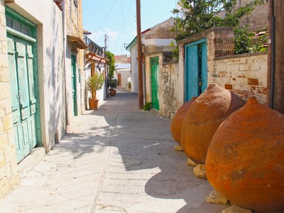 Smalle straat in een Cypriotisch dorp met stenen huizen, turquoise deuren en grote terracotta kruiken.