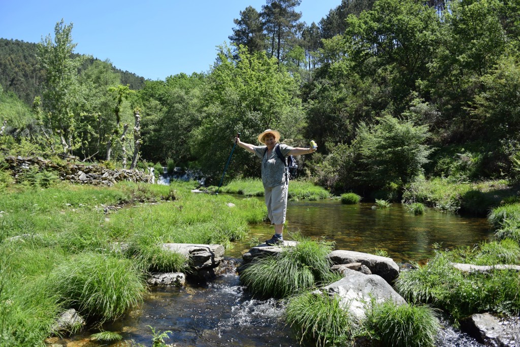 Wandelaar steekt een beek over via rotsen in groen landschap tijdens wandelvakantie in de Douro Vallei, Portugal.
