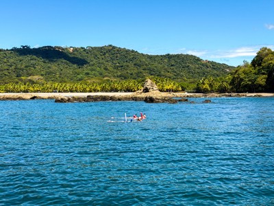 Snorkelaars in zee bij een tropisch strand aan de kust van Costa Rica, met palmen en groene heuvels op de achtergrond.
