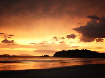 Zonsondergang aan het strand bij Phuket, Thailand, met silhouet van eiland en wolkenlucht.